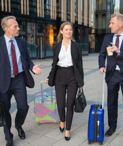 Confident businesspeople with luggage walking to hotel Confident businesspeople with luggage walking to hotel, wheeling suitcases, talking. Full length, front view. Business travel or corporate communication concept