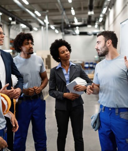 As you can see, we follow this working plan here! Young manual worker presenting new business strategy to company managers and his colleagues in a factory.